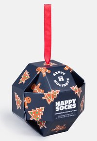 Caja de regalo hexagonal de color azul oscuro con muñecos de jengibre y árboles de Navidad, con una cinta roja colgante y un texto de marca en blanco.