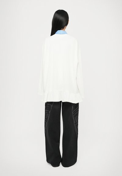 White long-sleeve top with ruffled hem paired with black wide-leg pants featuring textured geometric patterns on the sides.