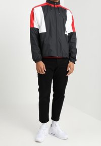 Pánská černá větrovka s červenými a bílými akcenty. Celý zip, vysoký límec, elastické manžety, stylizovaná s černými kalhotami a bílými teniskami.