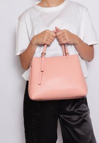 Borsa a tracolla in pelle testurizzata rosa con due manici, forma rettangolare e dettagli in hardware dorato. Indossata con una maglietta bianca e pantaloni scuri.