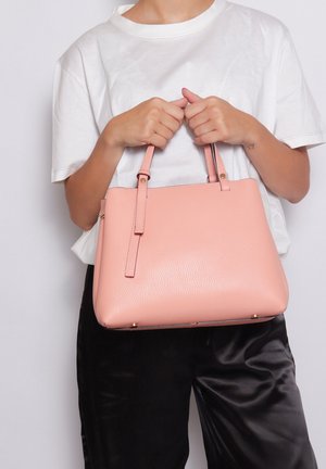 Roze leer handtas met textuur, twee handvatten, rechthoekige vorm en gouden hardware accenten. Draag het met een wit T-shirt en donkere broeken.