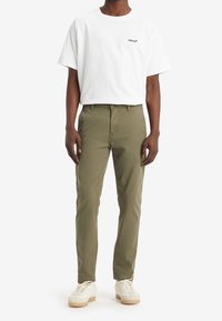 Bílá bavlněná tričko s logem "Levi's", spárované s olivově zelenými chinos kalhotami a bílými teniskami se světle béžovými podrážkami.