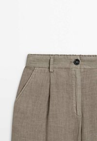 Pantalon léger en lin beige avec fermeture à boutons, plis sur le devant et poches latérales. Texture douce et design décontracté.