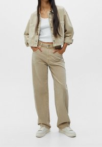 Veste en denim beige avec une coupe courte et une fermeture à bouton, associée à un pantalon beige taille haute. Portez-le avec des baskets blanches.