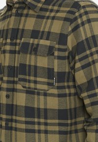Groene en zwarte geruite overhemden met een knoopsluiting, twee borstzakken en een geweven label aan de zijkant. Textuur van de stofafwerking.