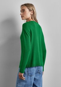 Grön stickad tröja med långa ärmar, rund halsringning och ribbad nederkant. Kombinerad med ljusblå högmidjade jeans. Synlig strukturerad tyg.