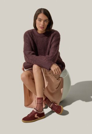 Maglione borgogna peloso, gonna di seta rosa, sneakers borgogna con suola in gomma e calzini a righe, il tutto disposto su uno sfondo grigio chiaro.