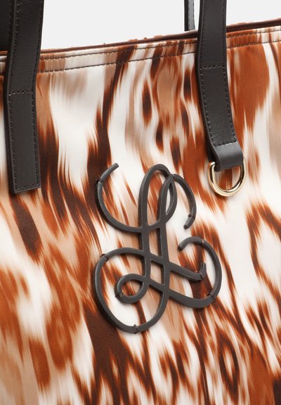 Close-up of brown and white patterned bag with black leather handles and twisted black logo detail stitched on the front.