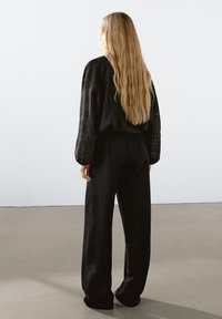 Černý, volný outfit s texturovaným, dlouhým rukávem a širokými kalhotami, oba vyrobené z lehké látky.