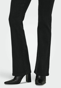Jeans de denim negros con un corte recto y un dobladillo deshilachado. Combinados con botines de tacón cuadrado negro de piel.