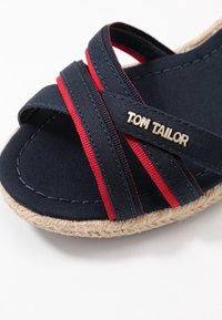 Sandales bleu marine avec des brides rouges accentuées, empiècement en textile et semelle en jute. Présente le logo "TOM TAILOR" en argent sur la bride.