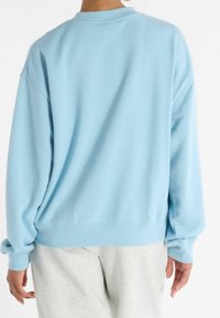 Person wearing a loose light blue sweatshirt and light gray sweatpants, viewed from the back against a plain white background.