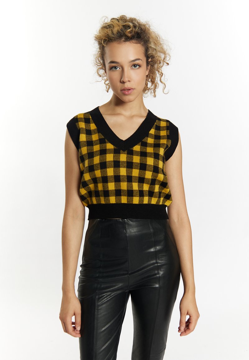 Sárga és fekete kockás kötött crop top V-kivágással és rövid ujjakkal, fekete, magas derekú bőrnadrággal párosítva.