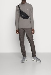 Schwarze Umhängetasche mit Markenlogo, graues Langarmshirt, grau karierte Hose und graue Turnschuhe. Fokus auf funktionalem, modernem Design.