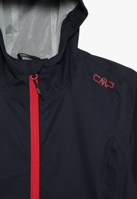 Giacca leggera nera con zipper rossa e logo CMP in alto a destra. Foderata in rete grigia, dotata di cappuccio e texture liscia.