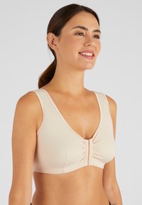 Beige zachte stoffen beha met een V-hals, brede bandjes, sluiting met haak aan de voorkant en geplooide details in het midden. Glad textuur overal.