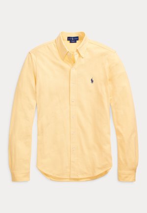 Żółta koszula na długi rękaw z zapięciem na guziki, kołnierzykiem zapinanym na guziki oraz małym granatowym haftowanym logo na lewym przodzie.