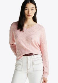 Maglione rosa a maglia grossa con scollo a V e maniche lunghe, abbinato a pantaloni bianchi a vita alta. Texture notevole e dettagli a coste.