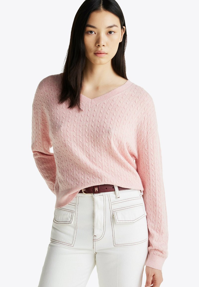 Maglione rosa a maglia grossa con scollo a V e maniche lunghe, abbinato a pantaloni bianchi a vita alta. Texture notevole e dettagli a coste.
