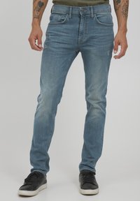 Jeans de mezclilla azul claro con un ajuste slim, que presentan un ligero desgastado y detalles rasgados, cinco bolsillos y cierre de botón.