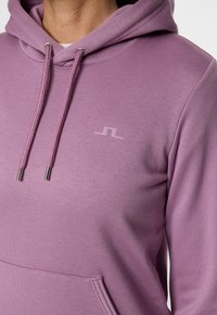 Felpa viola in morbido tessuto, con tasca a marsupio, cordini regolabili con punte metalliche e un piccolo logo sul petto.