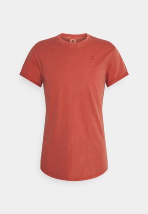 Kurzes rust-orangefarbenes T-Shirt mit Rundhalsausschnitt und dezentem Logo auf der linken Brust, dargestellt vor weißem Hintergrund.