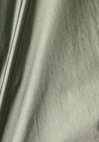 Metaliczna tkanina w odcieniu oliwkowym z gładką fakturą, delikatnym połyskiem i subtelnymi zmarszczkami, ukazująca lekkie i zwiewne cechy.