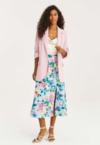 Světle růžový blazer, saténový bílý top, midi sukně s květinovým vzorem a rozparkem, béžové sandály na pásky, ukazující živé barvy a hladké textury.