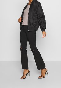 Černá bomber bunda s hladkým povrchem, spárovaná s pruhovaným tričkem, opranými černými zvonovými dž íny a černými sandály na podpatku s pásky.