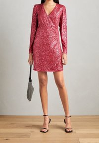 Rosa paljettklänning med långa ärmar, omlottdesign och V-ringning. Kombinerad med en svart nätväska och svarta klackar med remmar.