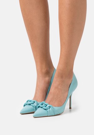 Un paio di tacchi alti a punta realizzati in pelle blu chiaro, con un accento decorativo a nodo sulla punta e sottili tacchi a stiletto.