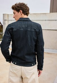 Dark denim jacket with a straight fit, featuring a classic collar, button closure, and silver hardware accents. Smooth texture, minimal details.