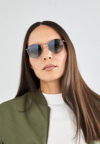 Occhiali da sole rotondi con lenti scure e montatura in metallo argentato. Le lenti sono leggermente riflettenti e il design presenta accenti minimalisti.
