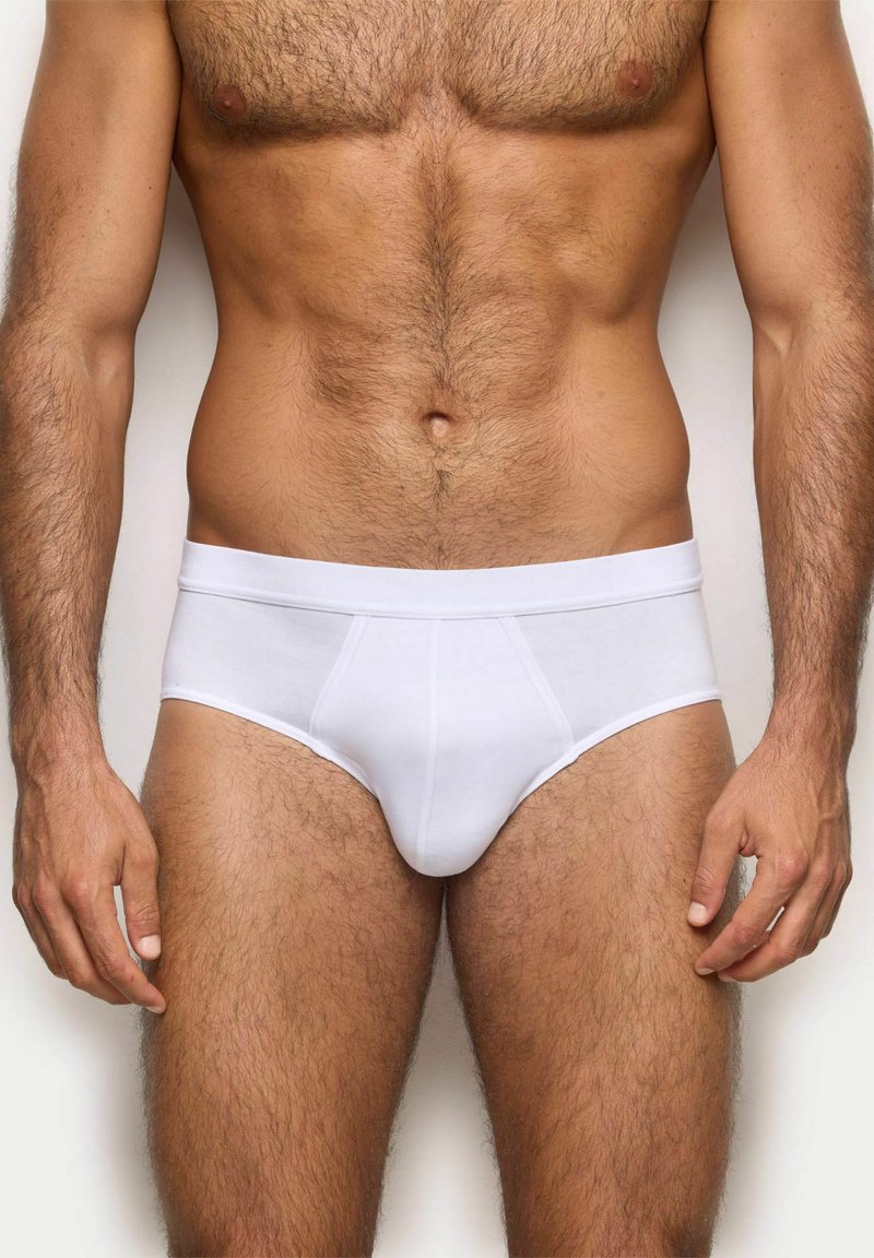 Slip di cotone bianco con una cintura morbida, caratterizzati da una vestibilità aderente e una superficie liscia. Design su misura con dettagli di cucitura minimi.