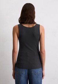 Donkergrijze geribbelde tanktop met een ronde halslijn en brede schouderbanden, gecombineerd met blauwe denim jeans met achterzakken.