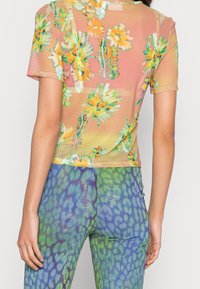 Gennemsigtig, kortærmet top i pink med flerfarvet blomsterprint; parret med blågrønne leggings med et struktureret, dyrelignende mønster.