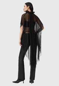Czarna, przezroczysta peleryna z subtelnymi błyszczącymi zdobieniami, falbankowany dekolt, w połączeniu z czarnymi dopasowanymi spodniami i czółenkami na szpilce.