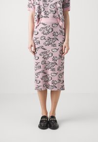 Gehaakte roze twee-delige set met een T-shirt met korte mouwen en een rok tot de knie, versierd met zwarte bloemen- en schelppatronen, aangevuld met glanzende zwarte instappers.