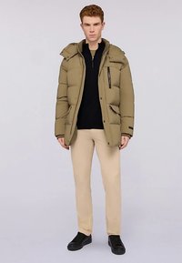 Prošívaná khaki bunda s kapucí, předním zipem na kapsu a viditelným šitím. Kombinováno s černým topem a béžovými kalhotami. Černé boty.