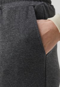 Grå bomulds sweatpants med en sidelomme, med et tekstureret stof og blød talje. En hånd hviler i lommen for skala.