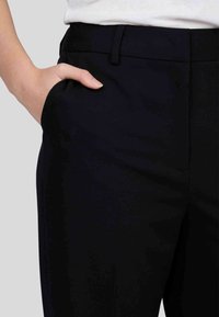 Pantalons de costume bleu marine avec une texture lisse, dotés d'une poche latérale et d'une coupe ajustée, conçus pour un look propre et professionnel.