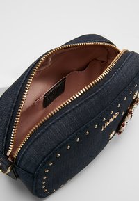 Borsa cosmetica in denim scuro con zip dorata, interna foderata in tessuto rosa chiaro. Presenta borchie decorative e accenti di gemme all'esterno.