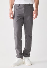 Pantalones de algodón gris con un diseño de pierna recta, que cuentan con bolsillos delanteros, cierre de botón y se llevan con zapatillas blancas.