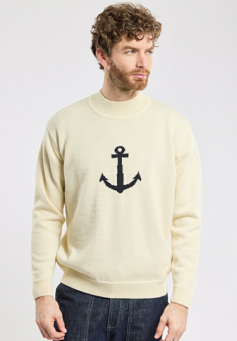 Pull en tricot couleur crème avec un motif d'ancre noire au centre, col et poignets côtelés, et coupe décontractée.