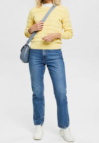 Keltainen neulottu paita, jossa vaakaraitoja, yhdistetty sinisiin suoralahkeisiin farkkuihin. Asusteina pieni sininen olkalaukku ja valkoiset tennarit.