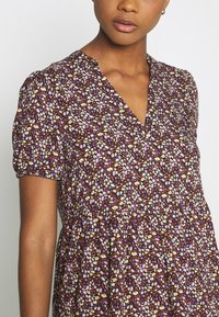 Blumenkleid mit tiefem V-Ausschnitt, kurzen Puffärmeln und geraffter Taille. Hat einen dunkelvioletten Grundton mit weißen, orangefarbenen und violetten Blumen.