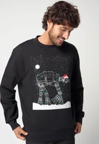 Felpa nera con graphic di un camminatore AT-AT, decorata con luci natalizie e un cappello di Babbo Natale, ambientata in un paesaggio notturno innevato.