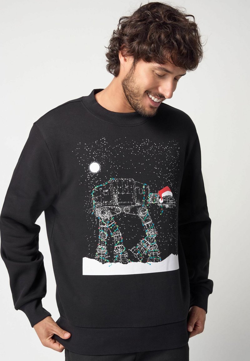 Felpa nera con graphic di un camminatore AT-AT, decorata con luci natalizie e un cappello di Babbo Natale, ambientata in un paesaggio notturno innevato.