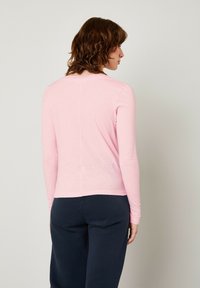 Camicia rosa a maniche lunghe con scollo rotondo, texture liscia, forma aderente e una cucitura centrale, abbinata a pantaloni blu scuro.