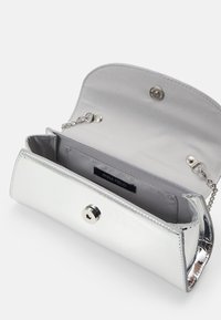 Clutch de charol plateado con cadena, que cuenta con un cierre de botón a presión y un interior de satén gris con una etiqueta de la marca.